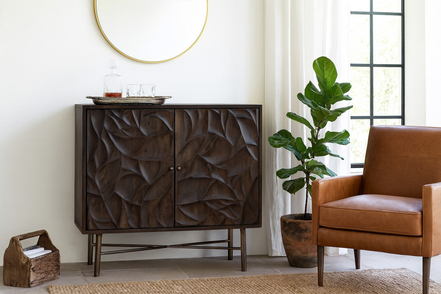 Dark wooden cabinet with leaf-patterned design in a room with a brown chair, plant, and round mirror.