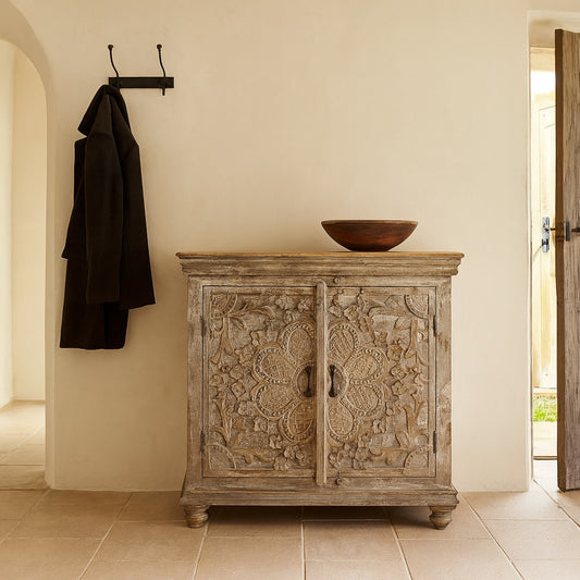 Decorative wooden cabinet with intricate carvings in a room with a coat hanging on a hook.
