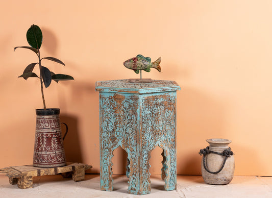 Decorative table with ornate carvings, fish sculpture, and vases against a peach background